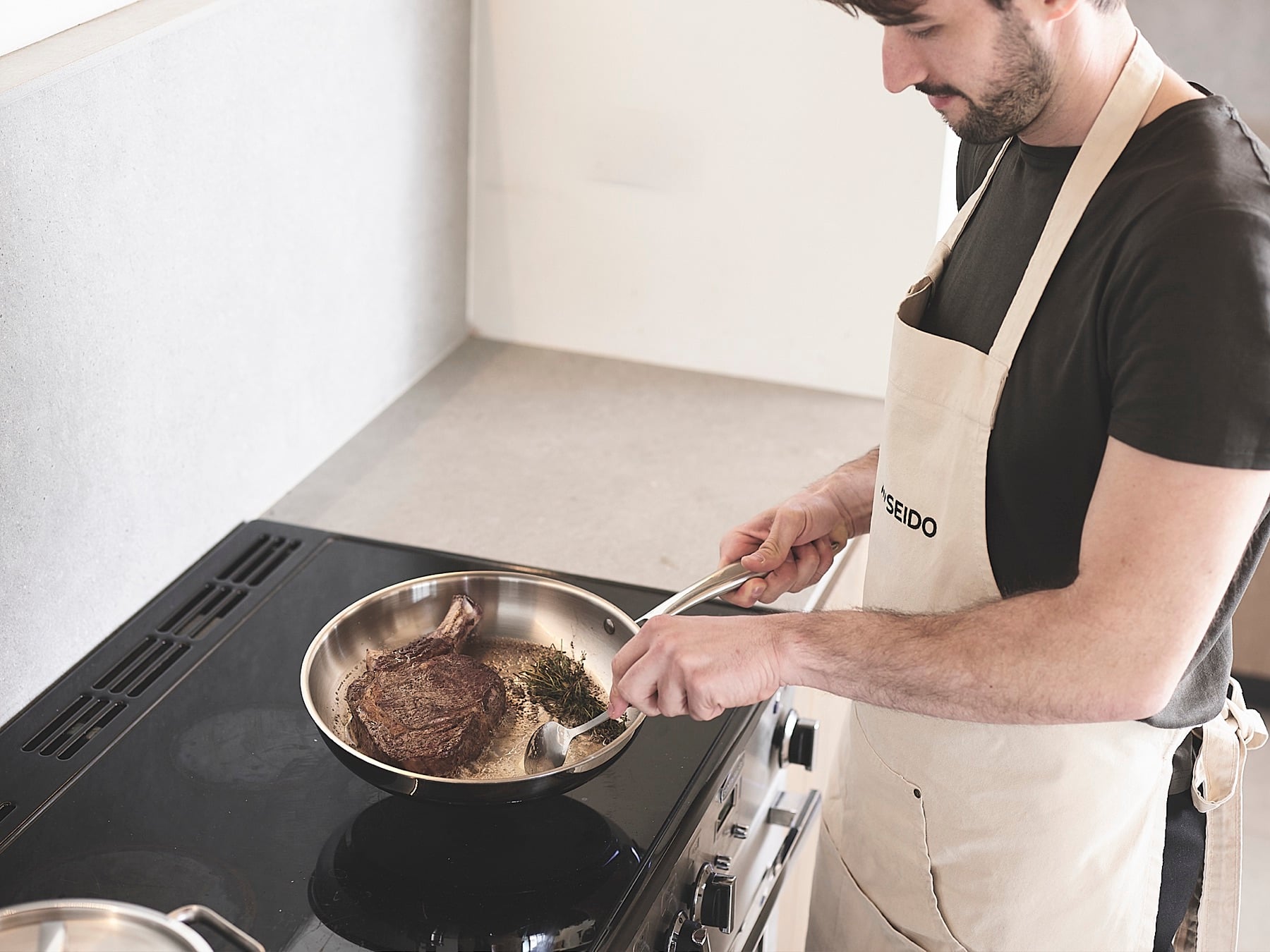 Steak searing in an uncoated stainless steel frying pan on the hob